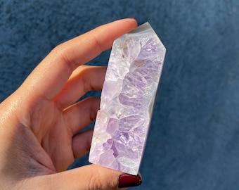 May include: A purple amethyst crystal point with a natural, raw, and textured surface. The crystal is translucent and has a light purple hue.
