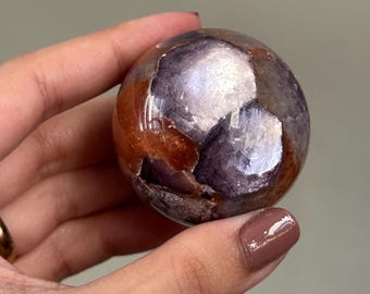 May include: A sphere of iridescent purple and orange lepidolite, a type of lithium mica, with a smooth, polished surface.