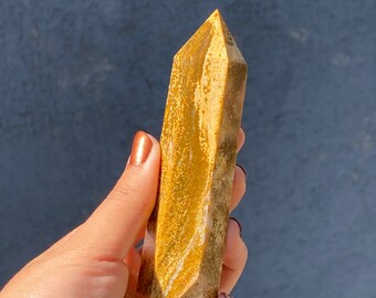 May include: A yellow and brown crystal point with a pointed tip. The crystal has a natural, rough texture and is a light brown color with streaks of yellow.