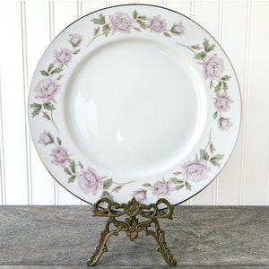 May include: A white porcelain dinner plate with a gold rim and a delicate floral design featuring pink roses and green leaves.