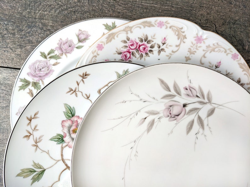 May include: Three white ceramic plates with floral designs. The top plate has a gold trim and a pink and brown floral pattern. The middle plate has a pink and green floral pattern. The bottom plate has a light pink and grey floral pattern.