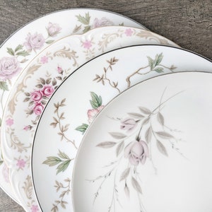 May include: Four white ceramic plates with floral designs in shades of pink and green. The plates are stacked on top of each other, with the largest plate at the bottom and the smallest plate at the top.