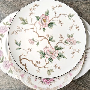 May include: Three white ceramic plates with a floral design. The top plate has a larger floral design with pink flowers and green leaves. The bottom two plates have a smaller floral design with pink flowers and green leaves.