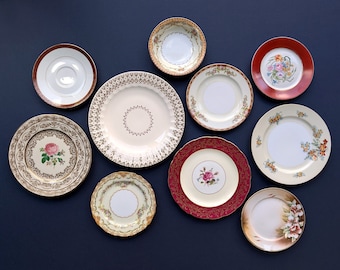 May include: A collection of ten vintage ceramic plates with floral and geometric designs in various colors, including white, gold, red, and brown. The plates are arranged in a circular pattern on a dark blue background.