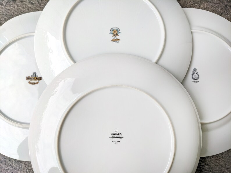 May include: Four white ceramic plates with gold trim and different logos. The logos include "Mikasa, Fine China, My Love", "Made in Japan", "Fine China", and "Made in Japan".