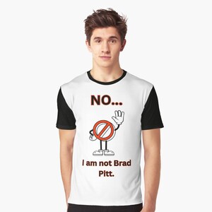 May include: White t-shirt with a black crew neck. The shirt has a graphic of a red circle with a diagonal line through it, with a stick figure with a hand raised in a stop gesture. The text "NO... I am not Brad Pitt." is printed below the graphic.