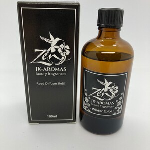 May include: A black and white box with a hummingbird and flower design. The box contains a 100 ml brown glass bottle of reed diffuser refill with the text "JK-AROMAS luxury fragrances Winter Spice."