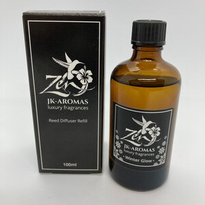 May include: A black box with a white hummingbird and flower design. The box says "JK-AROMAS luxury fragrances Reed Diffuser Refill 100ml". A brown glass bottle with a black cap and a white hummingbird and flower design. The bottle says "JK-AROMAS luxury fragrances Winter Glow".