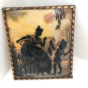 May include: A framed silhouette art piece depicting a woman and a child in a garden scene. The black silhouettes are set against a soft, colorful background. The frame is brown with gold accents, adding a vintage touch to the artwork.