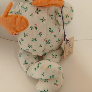 Pu&ograve; includere: Una bambola di peluche fatta a mano con un corpo in tessuto bianco a fantasia con foglie verdi e bacche rosse. La bambola ha accenti in feltro arancione e un'etichetta attaccata con uno spago viola. &Egrave; una decorazione festiva.