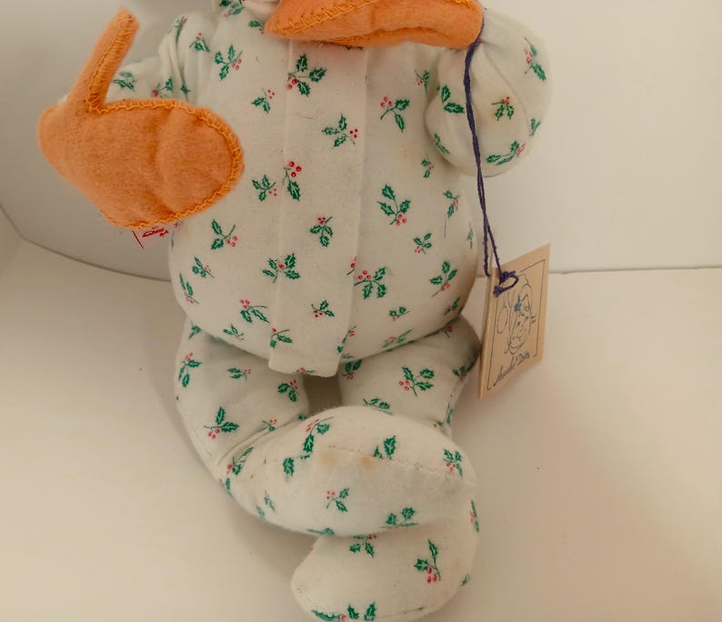 Pu&ograve; includere: Una bambola di peluche fatta a mano con un corpo in tessuto bianco a fantasia con foglie verdi e bacche rosse. La bambola ha accenti in feltro arancione e un'etichetta attaccata con uno spago viola. &Egrave; una decorazione festiva.