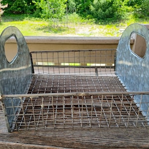 May include: A rectangular storage basket featuring a wire mesh base and sides, flanked by two solid, arched galvanized metal end panels. Each metal end panel includes a circular cutout handle at the top for carrying and organizing items.