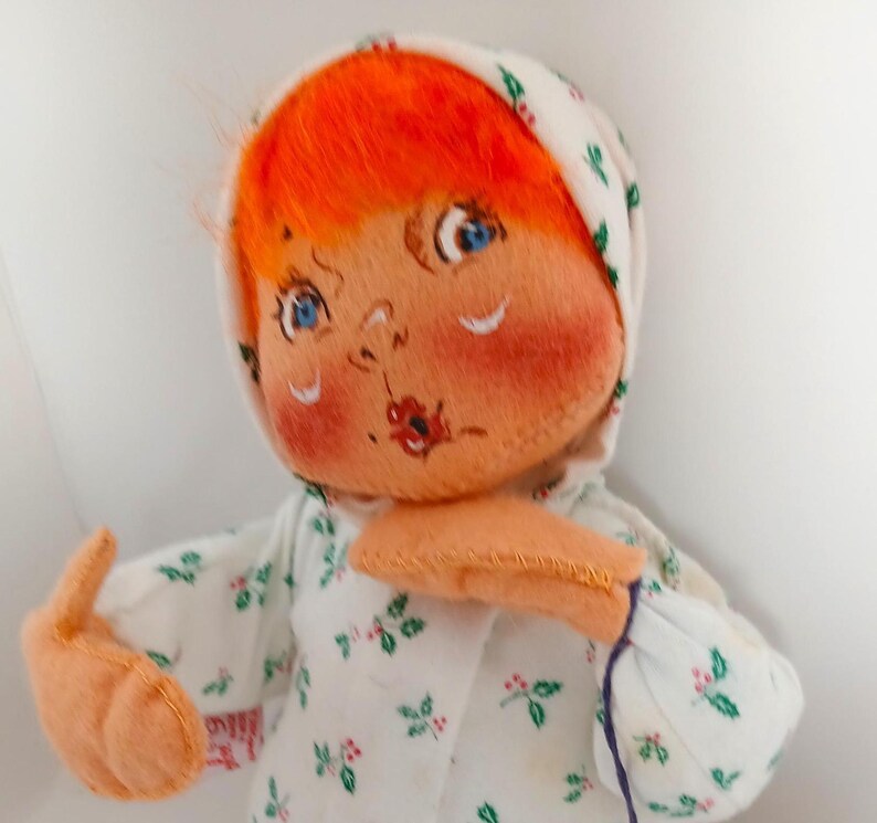 Pu&ograve; includere: Bambola fatta a mano con capelli arancioni, occhi blu e guance rosee. La bambola indossa un cappuccio bianco e un vestito bianco con un motivo floreale verde e rosso. Le braccia della bambola sono tese e il viso &egrave; dipinto a mano.