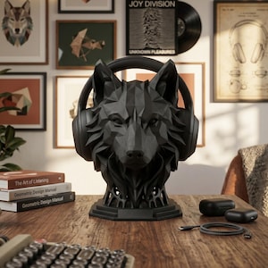 May include: A matte black, geometric wolf head sculpture serving as a headphone stand. The wolf bust features sharp, angular facets and is wearing a pair of black over-ear headphones. The base is octagonal, providing a stable foundation for the display.