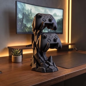May include: A black gaming controller stand shaped like a jagged rock formation, holding two black wireless game controllers. The stand features a textured, dark gray surface with sharp, angular edges, providing a stable base for the controllers.