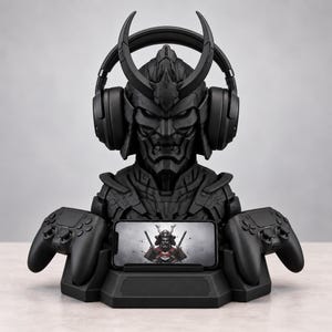 May include: A matte black gaming organizer stand shaped like a samurai bust wearing headphones. The base features two integrated controller docks on the sides and a central horizontal slot holding a smartphone displaying a samurai warrior graphic.