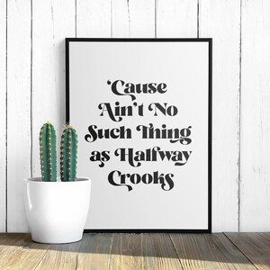 May include: Black and white typography print with the quote "'Cause Ain't No Such Thing as Halfway Crooks". The print is framed in a black frame and is displayed against a white wood background.