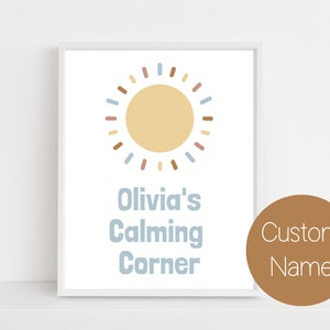 Może przedstawiać: Biały wydruk w ramie z żółtym słońcem z brązowymi i niebieskimi promieniami. Tekst pod słońcem brzmi "Olivia's Calming Corner".