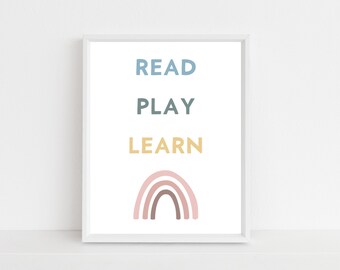 Könnte beinhalten: Ein weißer gerahmter Druck mit den Worten "READ PLAY LEARN" in blauem, grünem und gelbem Text. Ein rosa, brauner und beiger Regenbogen befindet sich am unteren Rand des Drucks.