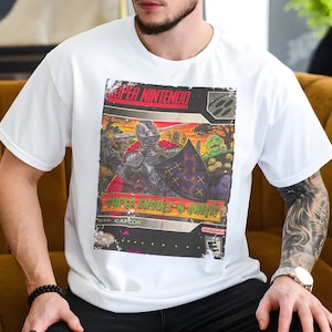 Könnte beinhalten: Weißes T-Shirt mit einem Vintage-Grafikdruck einer Super Nintendo-Spielkassette mit einem Ritter und dem Text "Super Ghouls 'n Ghosts".