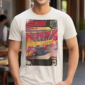 Può includere: Maglietta bianca con un design vintage di cartuccia di videogioco Super Nintendo che presenta un gioco di corse futuristico chiamato "F-Zero" con uno schema di colori rosso, blu e giallo.