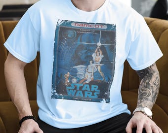 Puede incluir: Camiseta azul claro con un gráfico vintage de Star Wars. El gráfico incluye el texto "STAR WARS" y texto japonés. El diseño es de estilo póster de película retro con colores azules y blancos.