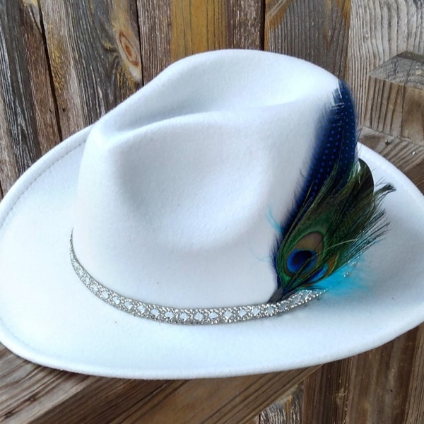 Unique white hat adorned with rhinestone hat band and peacock feathers, red underbrim.