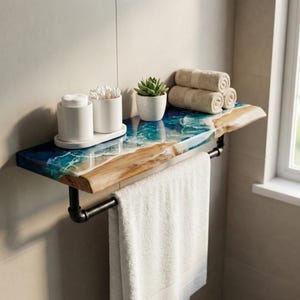 Könnte beinhalten: Badezimmerregal mit einer Baumkante und einem blau-weißen Epoxidharz-Wellenmuster. Das Regal enthält eine schwarze Handtuchstange, weiße Handtücher und weiße Keramikbehälter für Wattestäbchen und Wattepads. Eine kleine Sukkulente in einem weißen Topf und gerollte Handtücher befinden sich ebenfalls auf dem Regal.