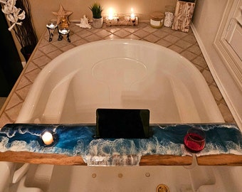 May include: A white bathtub with a wooden tray featuring a blue and white resin ocean wave design. The tray has a built-in tablet holder and a glass of wine. The tray is placed over the bathtub. The text "LIVE in the MOMENT" is visible on a framed picture hanging on the wall.