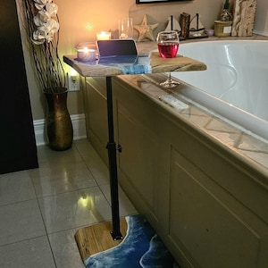 May include: A wooden bath tray with a black adjustable stand. The tray features a blue and white wave design. A framed sign with the words "LIVE in the MOMENT" hangs on the wall.