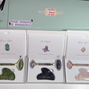 May include: Three boxes each containing a facial roller and a gua sha tool. The boxes are labeled "Green Jade", "Amethyst", and "Rose Quartz". Each box has a card with a crystal illustration and the words "Free Spirit Lifestyle".