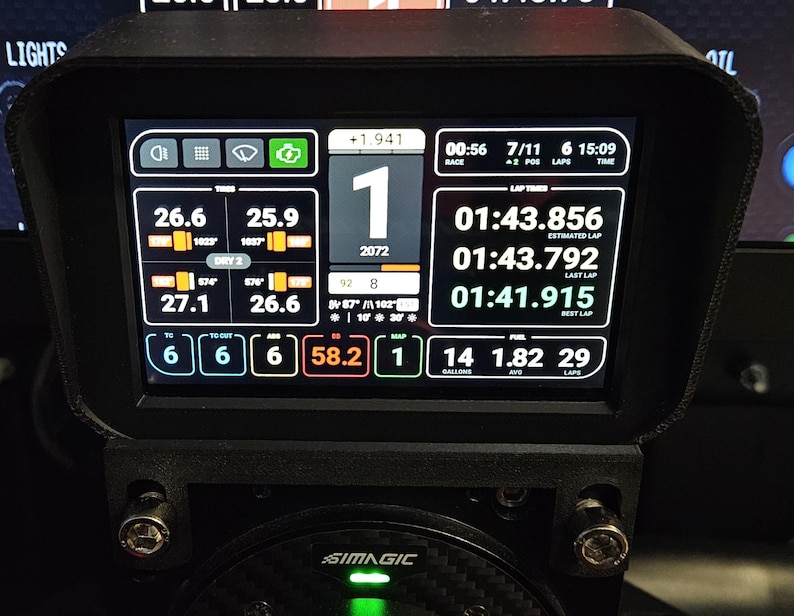 May include: A black racing simulator dashboard with a digital display showing race data, including lap times, fuel levels, and tire temperatures. The display also shows the driver's position, lap number, and race time. The dashboard is labeled "SIMAGIC".