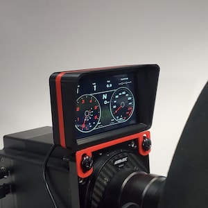 May include: A black racing wheel with a red and black screen mount. The screen displays a digital dashboard with a speedometer, tachometer, and gear indicator. The screen is labeled "SimuLogic".