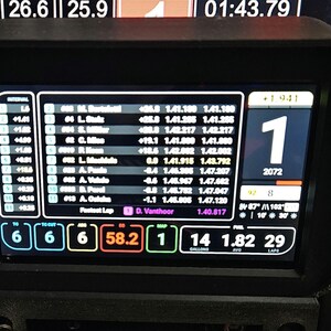 May include: A black and white digital display shows a race car dashboard with a large number "1" in the center. The display shows the car's position, lap time, and other race data. The display also shows the driver's name, "D. Vanthoor", and the car's number, "2072".