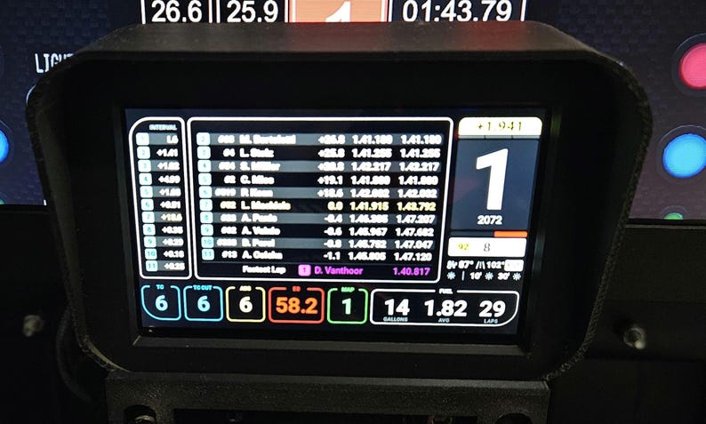 May include: A black and white digital display shows a race car dashboard with a large number "1" in the center. The display shows the car's position, lap time, and other race data. The display also shows the driver's name, "D. Vanthoor", and the car's number, "2072".