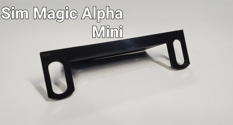 May include: Black plastic bracket with two oval-shaped holes on each side. The bracket is designed to hold a device, such as a phone or tablet, in place. The text "Sim Magic Alpha Mini" is visible in the image.