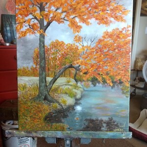 K&ouml;nnte beinhalten: &Ouml;lgem&auml;lde einer Landschaft mit einem Baum mit leuchtend orangefarbenen Bl&auml;ttern, die sich in einem blau-gr&uuml;nen Gew&auml;sser spiegeln. Das Kunstwerk, signiert mit "LINDA", zeigt eine Herbstszene unter bew&ouml;lktem Himmel.