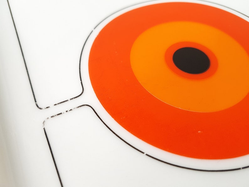 Pu&ograve; includere: Un vassoio da portata bianco in stile retr&ograve; con un audace design circolare arancione e nero. Il vassoio presenta una serie di cerchi concentrici arancioni, giallo-arancio e neri. Il vassoio ha una forma simile a una maniglia sul lato.