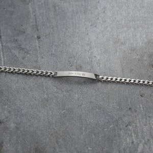 May include: A silver bracelet with a curb chain. The rectangular bar is engraved with the words "Her King" and a crown symbol. The bracelet is shown on a grey surface.