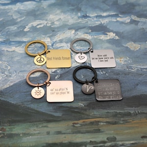 May include: Four different keychains with engraved square tags and round charms. The keychains are gold, silver, rose gold, and black. The tags have the following text: "Best Friends Forever", "Drive safe! Let me know you're safe. I love you!", "44° 44.4830' N 110° 40.3690' W", and "You are worth every mile between us and we love you to the moon and back".