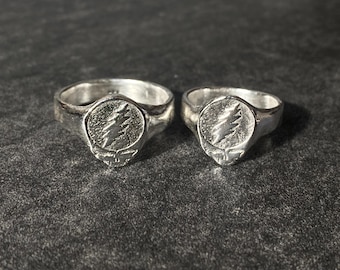 May include: Two silver rings featuring a stylised tree design. Both rings are plain bands with a raised design on the top.