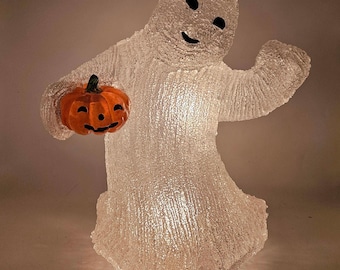 May include: A clear, textured ghost figure holding an orange pumpkin with a carved face. The ghost has black eyes and a smiling mouth. The Halloween decoration is illuminated and stands upright.
