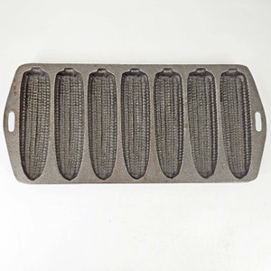 May include: Cast iron cornbread pan with eight individual molds shaped like corn cobs. The pan is gray and has a rustic, vintage look.