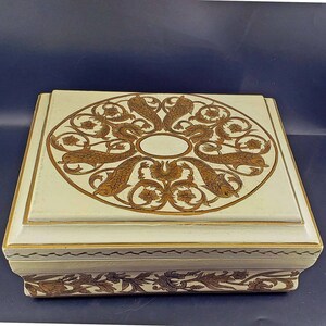 May include: A rectangular, off-white decorative box with a hinged lid. The lid features a circular design of stylized fish and floral elements in brown. The box has gold trim and additional brown floral patterns around the base.
