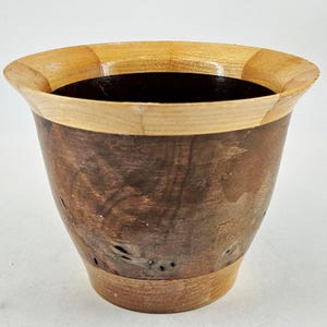 May include: A handcrafted wooden bowl with a flared rim. The bowl features a dark brown body with a light brown rim and base. The interior is a dark, contrasting color. The wood grain is visible, adding to the natural aesthetic.