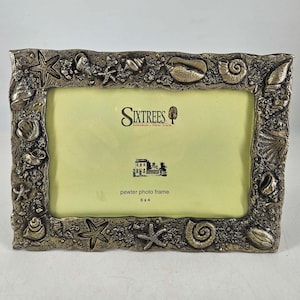 May include: A silver pewter photo frame with a seashell design. The frame is 6x4 inches and has the text "Sixtrees" and "pewter photo frame" on it.