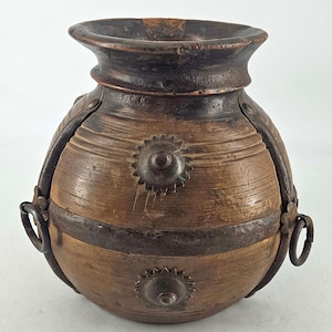 May include: A rounded wooden vessel featuring a dark brown finish, reinforced with dark metal bands and circular metal rings on the sides. The exterior is decorated with several star-shaped metal studs and has a wide, flared opening at the top.