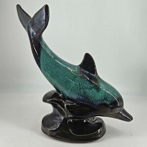 May include: A ceramic dolphin figurine with a black and green glaze. The dolphin is leaping out of the water and has a black base.