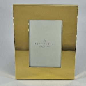 May include: A gold-colored rectangular picture frame with a white interior. The frame has a simple, classic design and features the text "POTTERY BARN classic frame 4 x 6 inches".