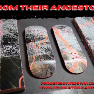 May include: Five fingerboards made from recycled skateboard decks. The fingerboards are black with orange and white paint splatter designs. The fingerboards are arranged in a row on a dark surface.